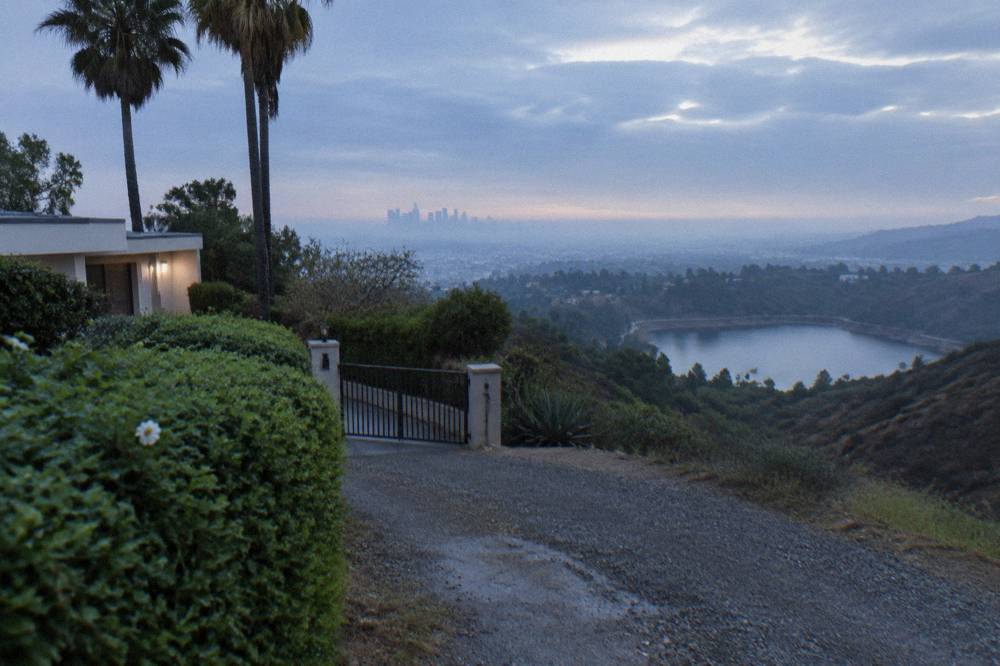 A gated driveway and manicured hedge along a hillside street above Sunset Boulevard