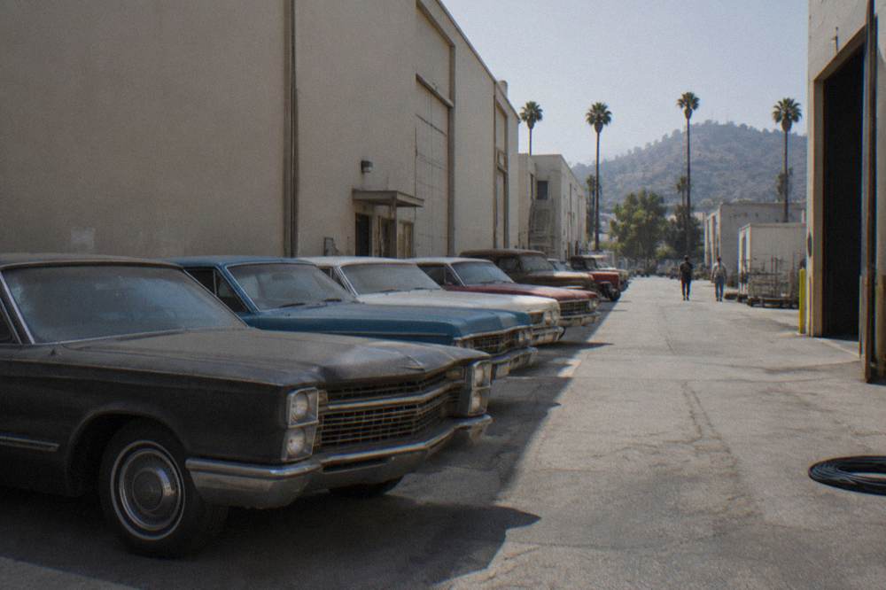 Rows of studio prop cars parked on a backlot under tall stage walls