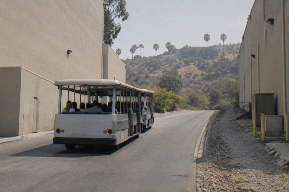Theme park tram vehicle climbing a hill between soundstage buildings