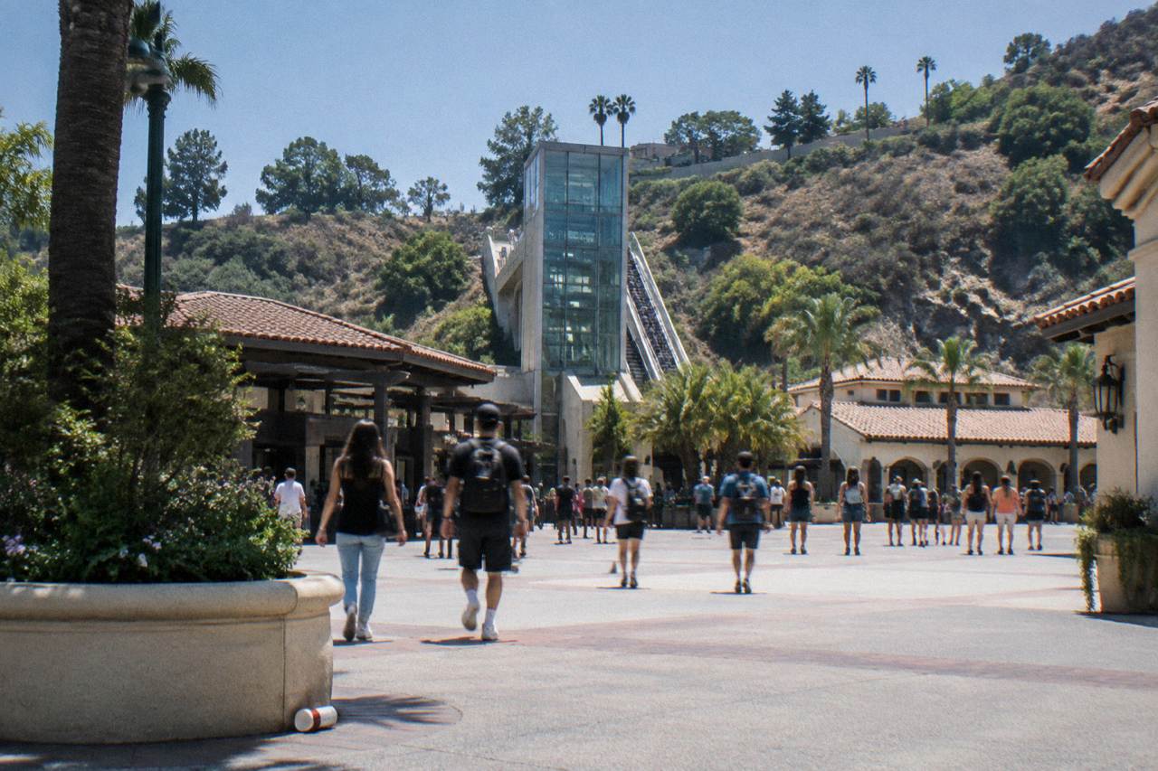 Entrance plaza of a theme park with a glass escalator rising toward a hillside under a clear sky
