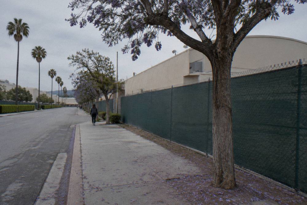 A quiet Culver City sidewalk outside a studio wall with a soundstage visible behind the fence