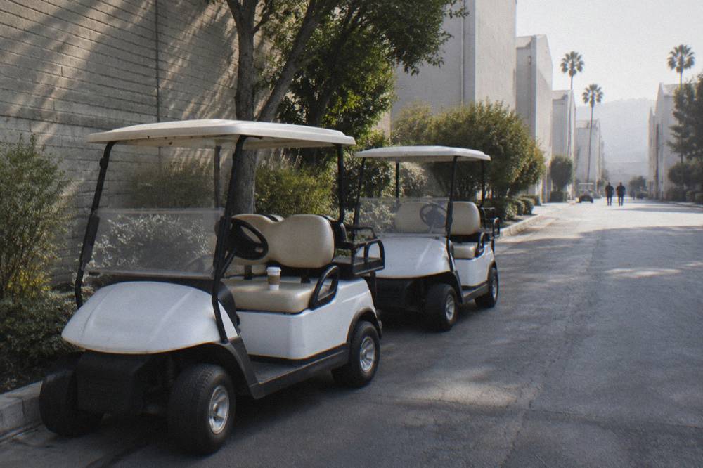 Two studio golf carts parked on a quiet lot road beside a painted soundstage wall