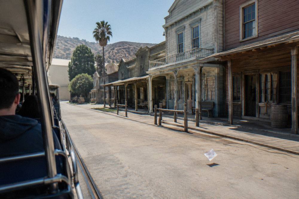 An open-sided studio tour tram passing painted western street facades on a backlot