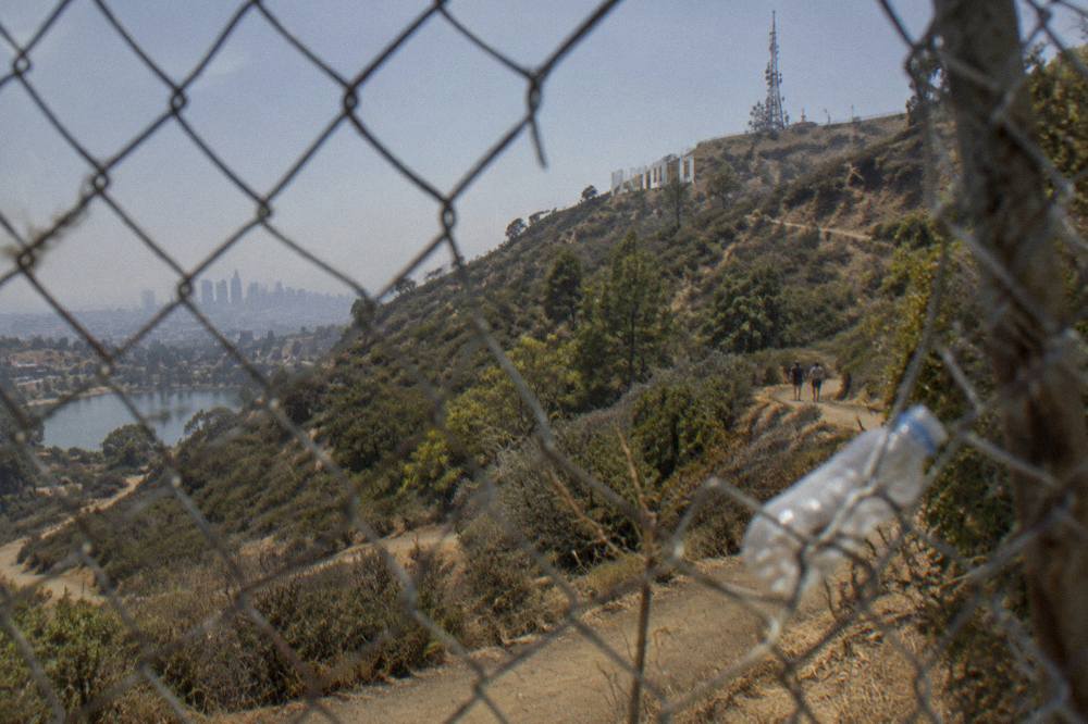 The Hollywood Sign seen from behind a chain-link fence on a hillside trail.