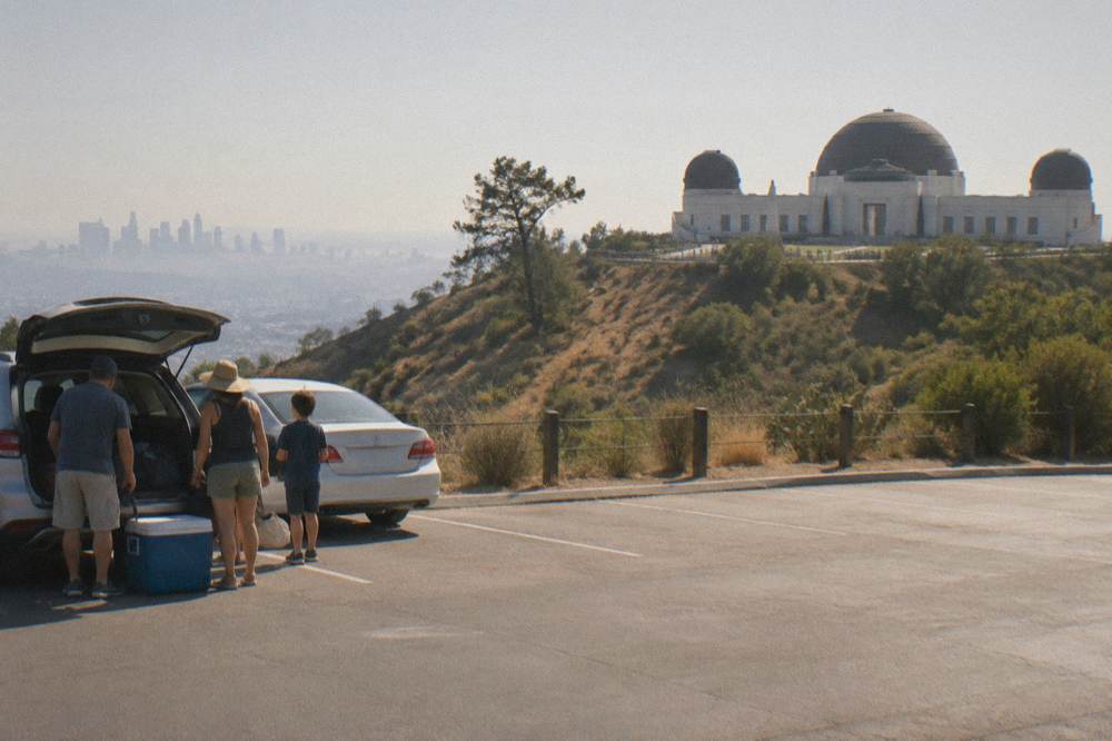 A parking lot at Griffith Observatory with cars and the Hollywood Sign in the background.