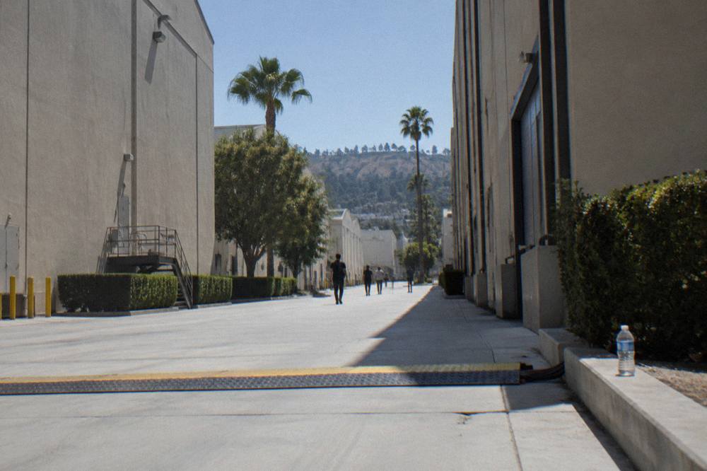A wide concrete pathway between two tall soundstage buildings on a studio lot