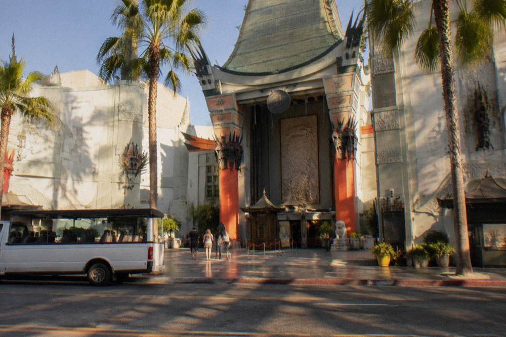 Tour van parked on a sunny Hollywood street beside a landmark theater facade