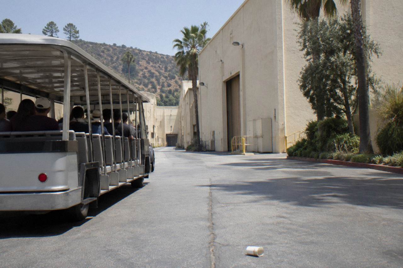 Open tour tram passing a soundstage facade on a sunny studio backlot