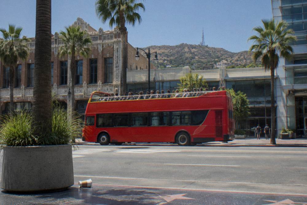 Open-air sightseeing bus passing along Hollywood Boulevard with the Hollywood Hills in the background