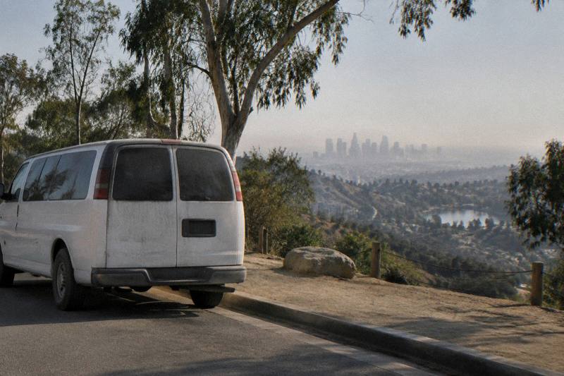 A tour van parked on a Hollywood Hills street overlooking a hazy Los Angeles skyline