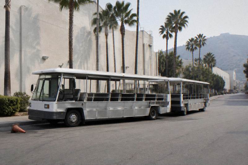 Numberless soundstage exteriors with a parked tour tram and palm trees along a quiet road on a Burbank studio lot