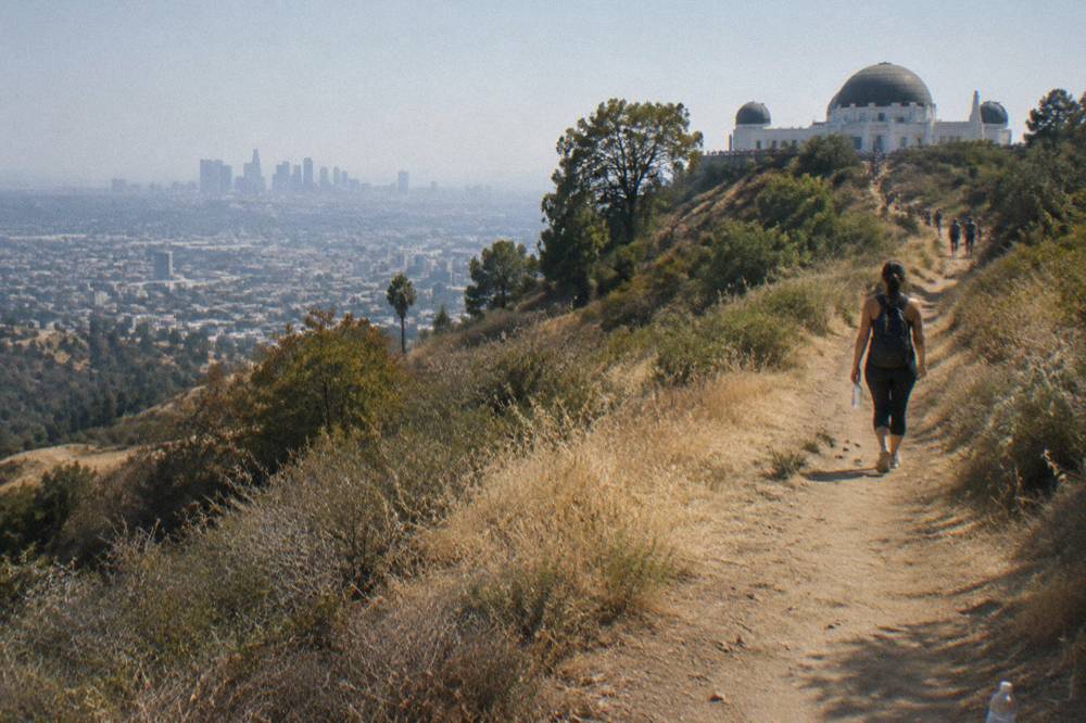 Hillside dirt trail rising through dry golden grass toward a ridge overlooking a wide city basin
