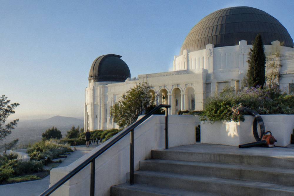 White art deco observatory building on a hillside with terraces overlooking a hazy city plain
