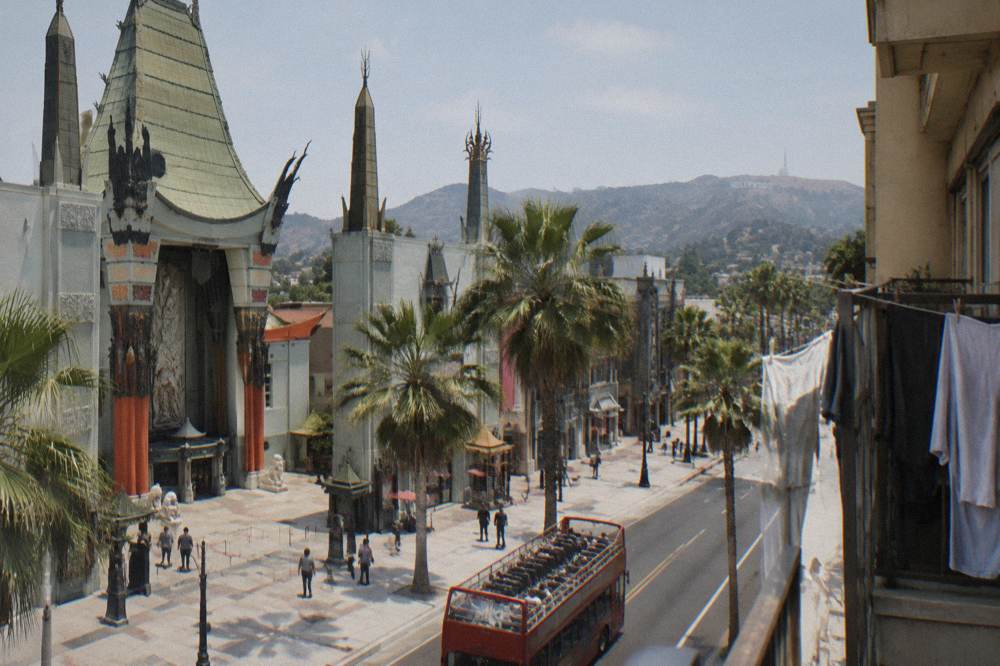 A tour bus driving along a palm-lined street with hills and the outline of the Hollywood Sign in the distance