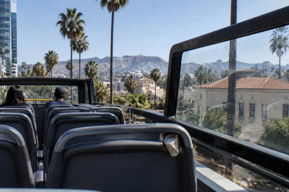 A tour bus interior with rows of seats and large windows facing city views