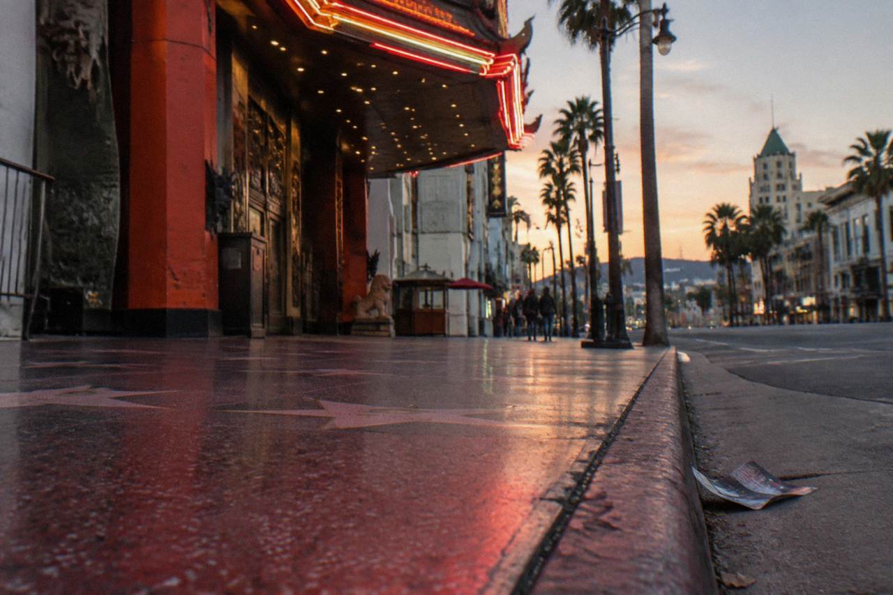 A vintage neon cinema marquee glowing above an empty Los Angeles sidewalk at dusk
