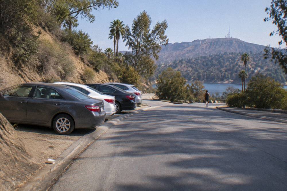 Cars parked along a curved hillside road below the Hollywood Sign hillsides in morning light