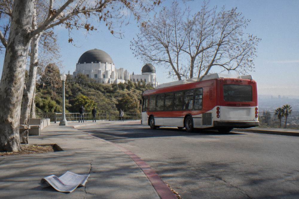 A city shuttle bus at a hillside stop with the Griffith Observatory dome above the trees