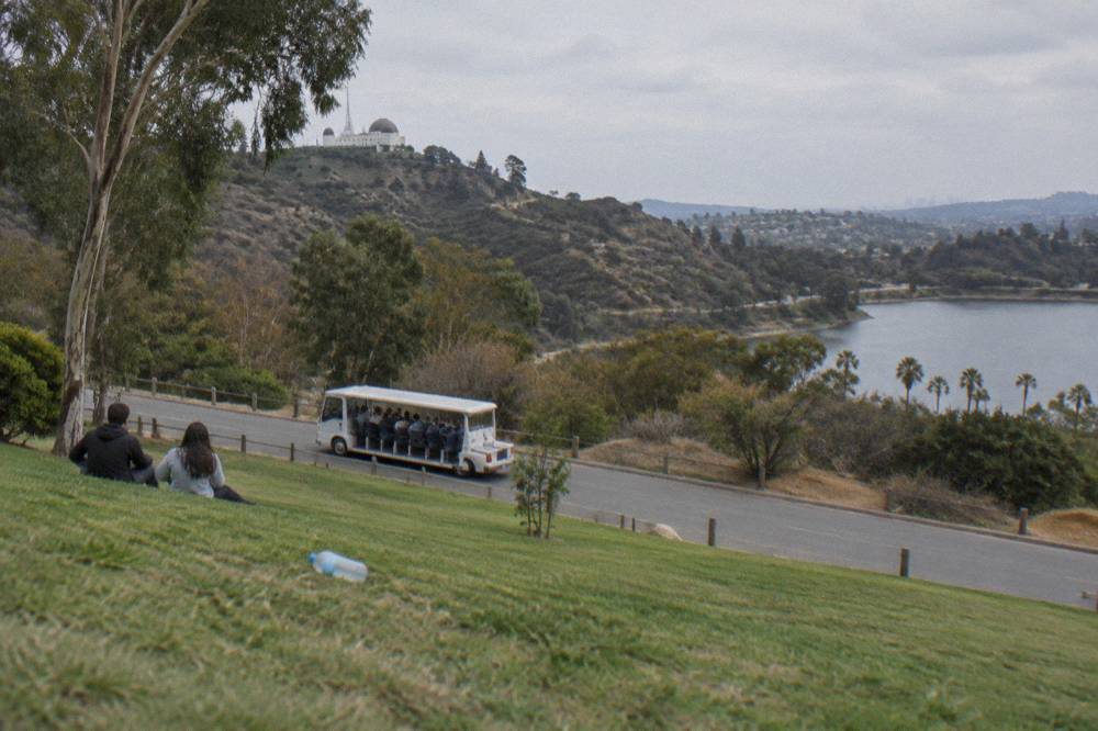 An open tour vehicle on a Hollywood hillside road with the sign on the ridge beyond