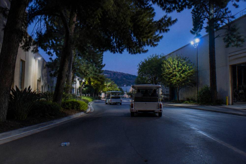 Two studio tour carts passing on a tree-lined lot road between soundstages