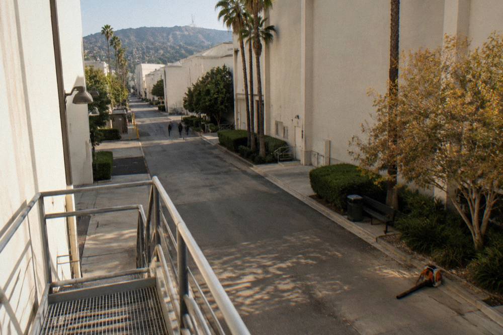 A quiet studio lot street with soundstage walls under late morning sun