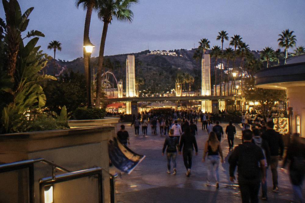A theme park entrance plaza lit for a nighttime event with crowds moving toward gates