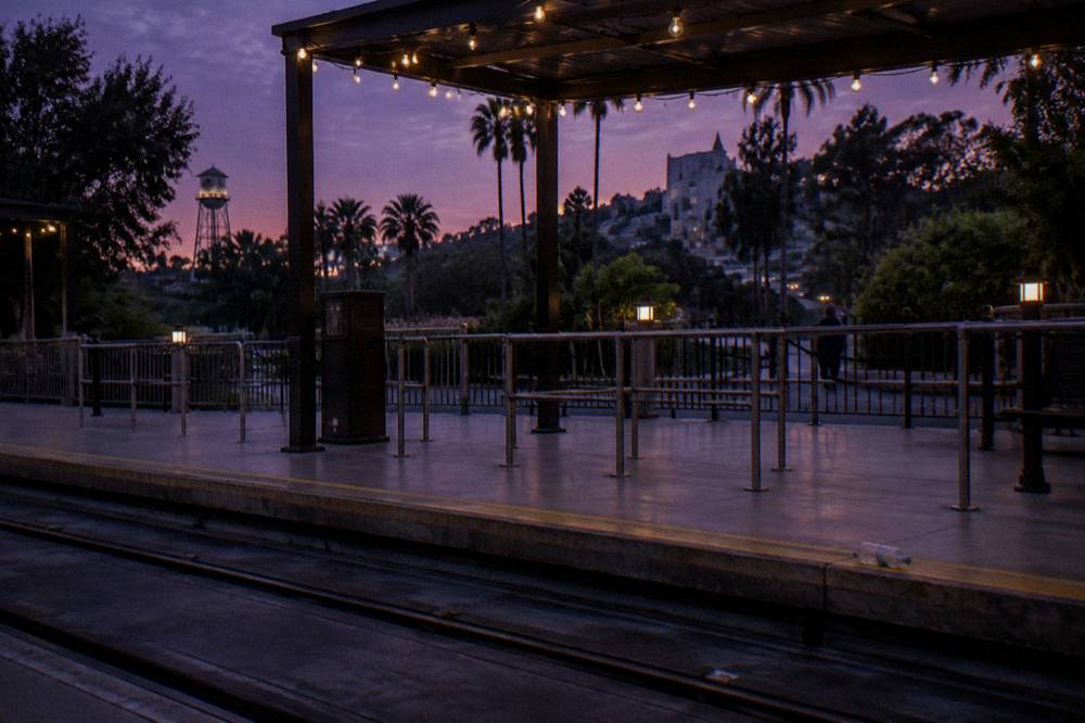 An outdoor tram loading area at a theme park at dusk with string lighting overhead