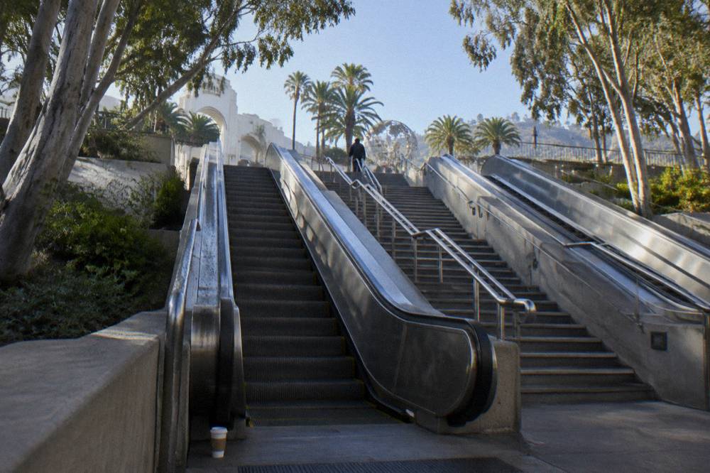 Entrance plaza escalators rising toward a theme park gate with crowds-free morning light