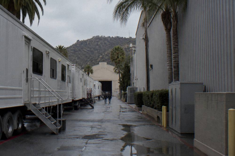 Quiet backlot alley with parked production trailers and stage walls