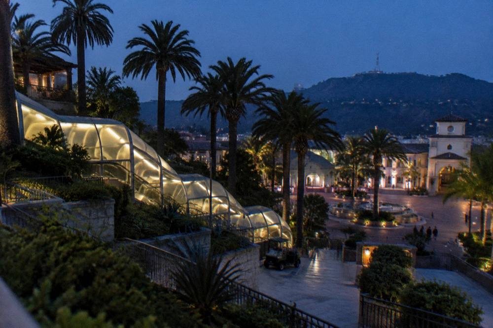 Theme park entrance plaza at dusk with escalators and hillside terraces