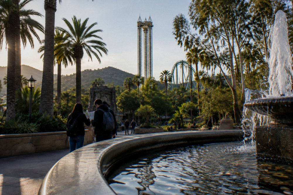 Family group studying a park map at a plaza fountain with ride towers behind