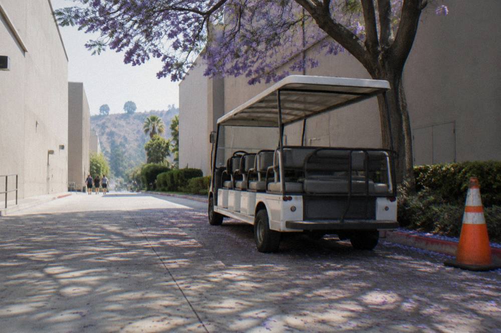 Guided tour cart parked on a tree-lined street between studio soundstages